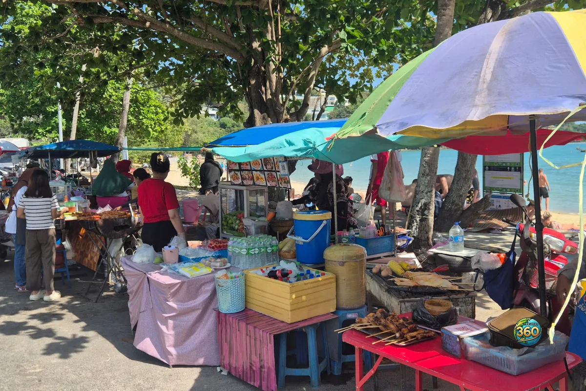 Stands de street food installés sous les arbres près d’Ao Yon Beach à Phuket, avec la mer visible en arrière-plan