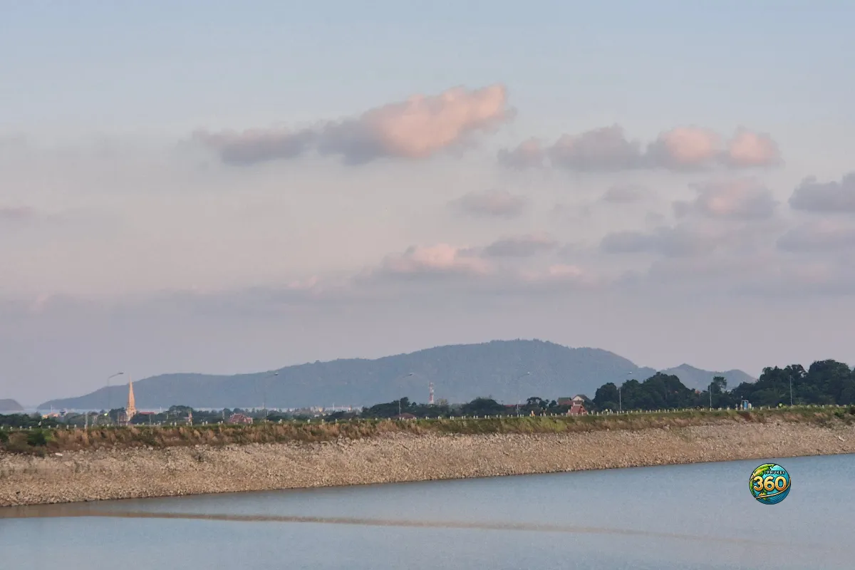 Vue sur le lac de Chalong Dam Reservoir à Phuket avec digue rocheuse, collines en arrière-plan et ciel pastel