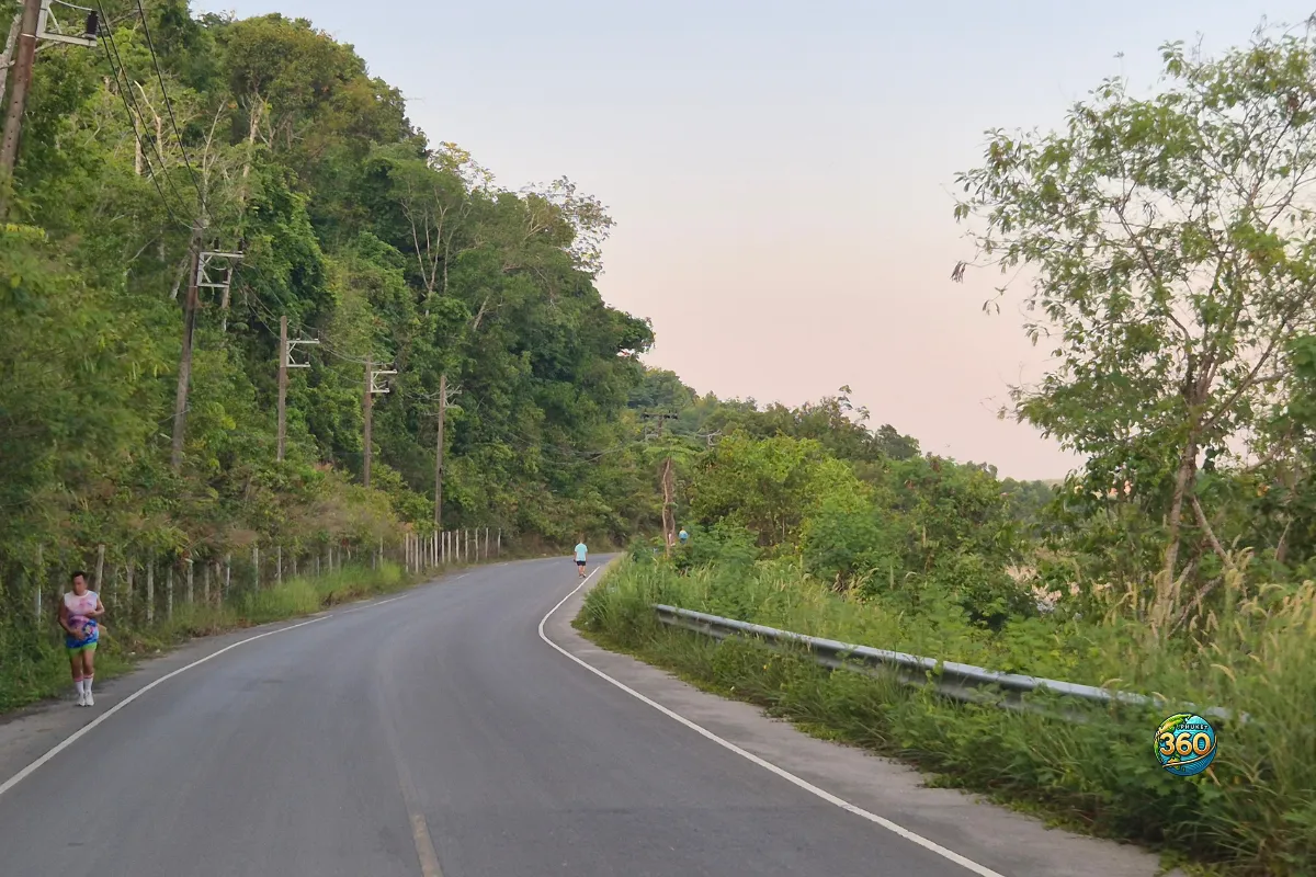Route près de Chalong Dam Reservoir à Phuket avec coureurs, végétation dense, poteaux électriques et ciel pastel