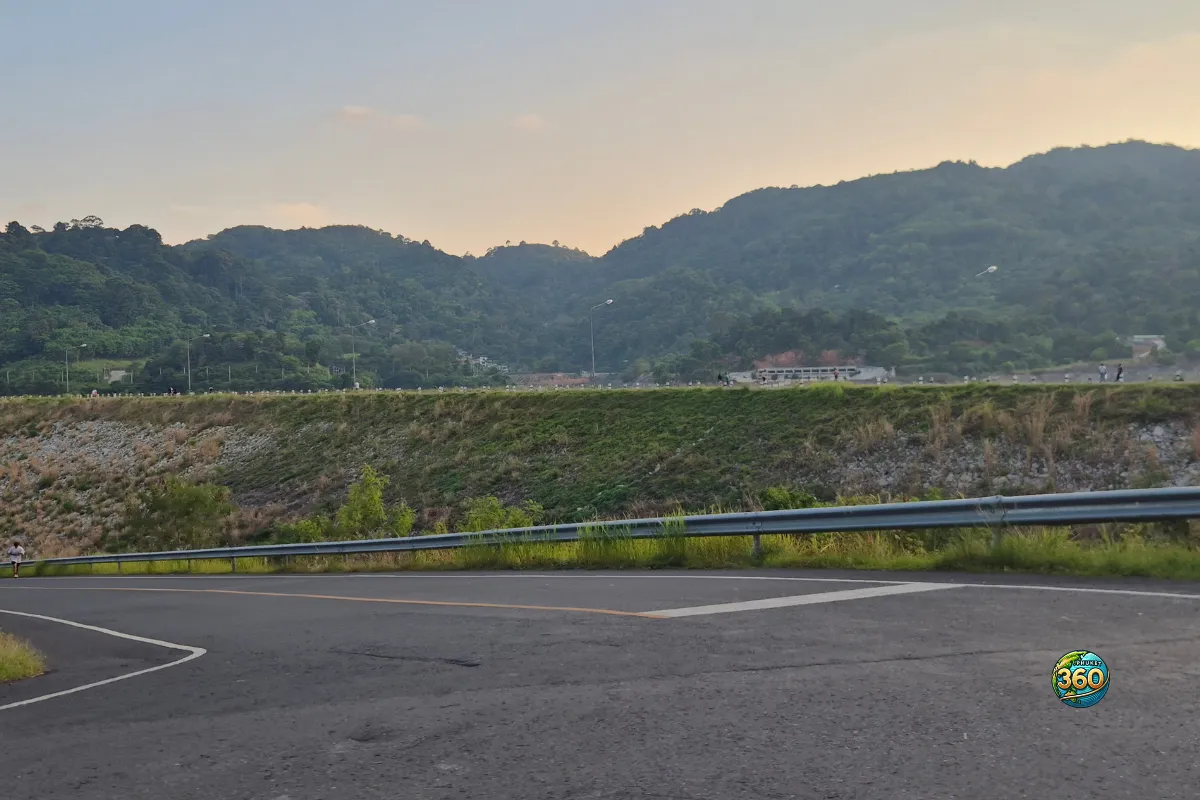 Virage de route près de Chalong Dam Reservoir à Phuket avec glissière, digue végétalisée et collines boisées