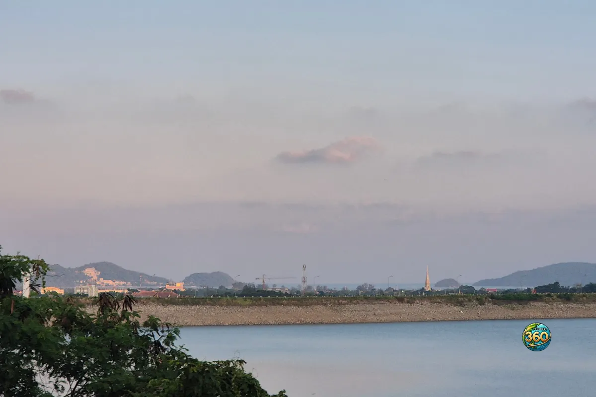 Vue sur le lac de Chalong Dam Reservoir à Phuket avec végétation au premier plan, collines en arrière-plan et ciel pastel