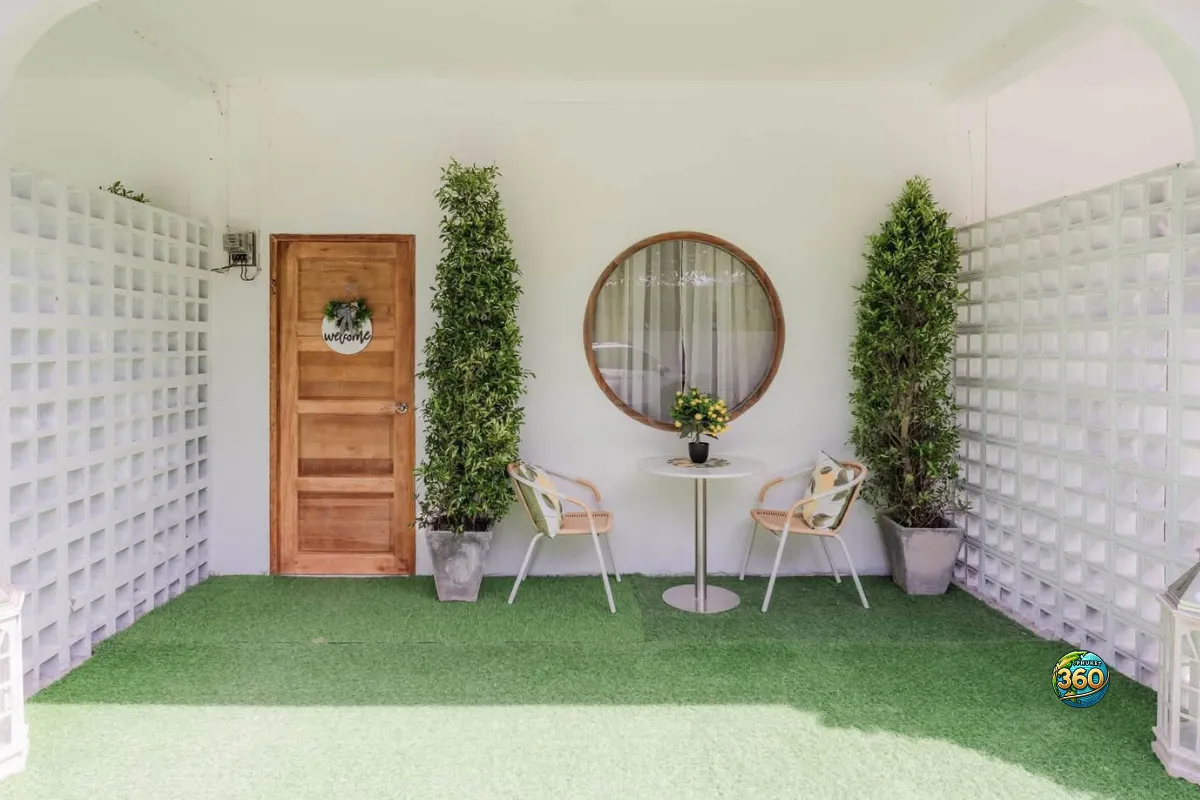 Entrée extérieure d’une chambre à louer à Phuket avec porte en bois, terrasse couverte, table ronde, chaises et plantes décoratives