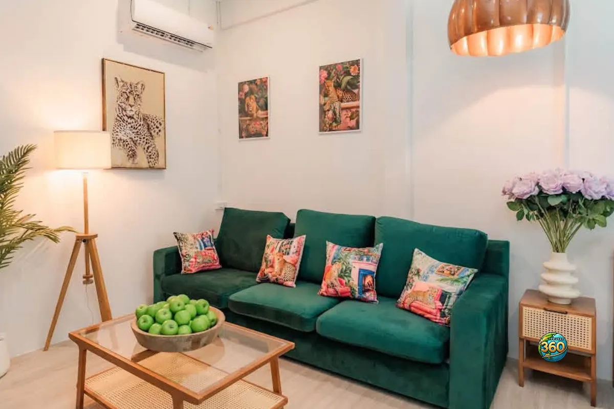 Salon décoré d’une chambre à louer à Phuket avec canapé vert, table basse, lampe, climatisation et décoration tropicale
