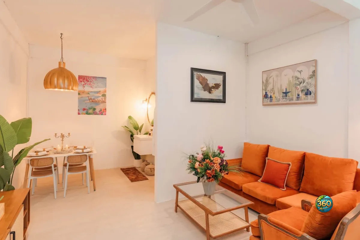Espace salon et coin repas d’une chambre à louer à Phuket avec canapé orange, table basse, décoration murale et salle à manger