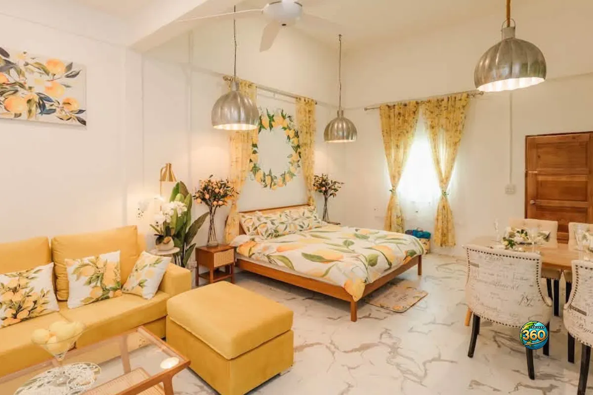 Studio lumineux à louer à Phuket avec lit double, canapé jaune, table à manger, rideaux jaunes et décoration citronnée
