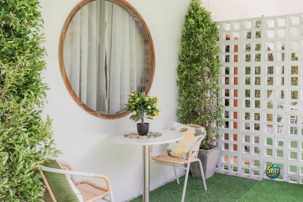 Terrasse d’entrée d’une chambre à louer à Phuket avec table ronde, deux chaises, miroir mural, plantes et sol en gazon synthétique