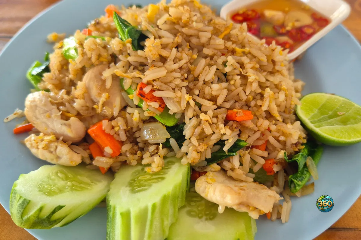 Assiette de khao pad gai avec riz sauté au poulet, œuf, légumes, concombre, citron vert et sauce au piment