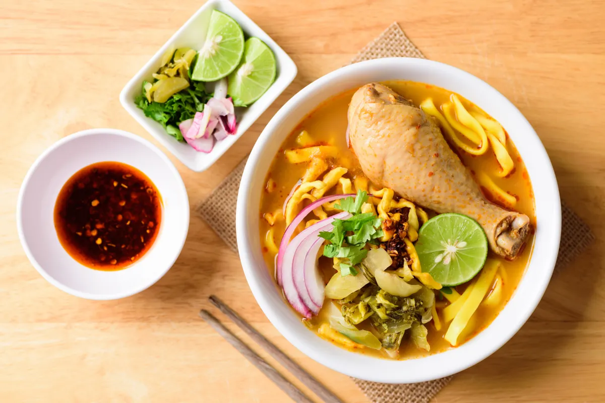 Bol de khao soi gai avec nouilles au curry, pilon de poulet, citron vert, oignon rouge, herbes fraîches et sauce pimentée