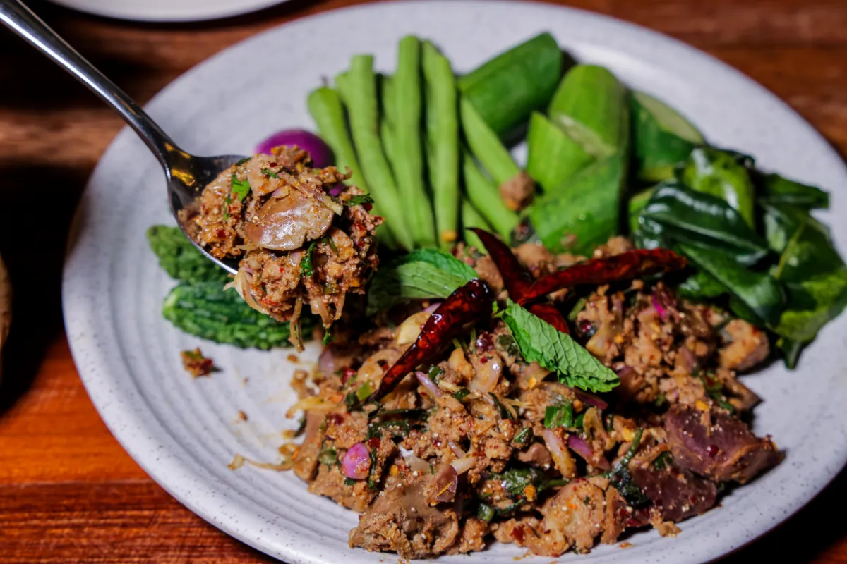 Assiette de larb thaï avec viande hachée épicée, herbes fraîches, piments séchés, concombre, haricots longs et feuilles vertes