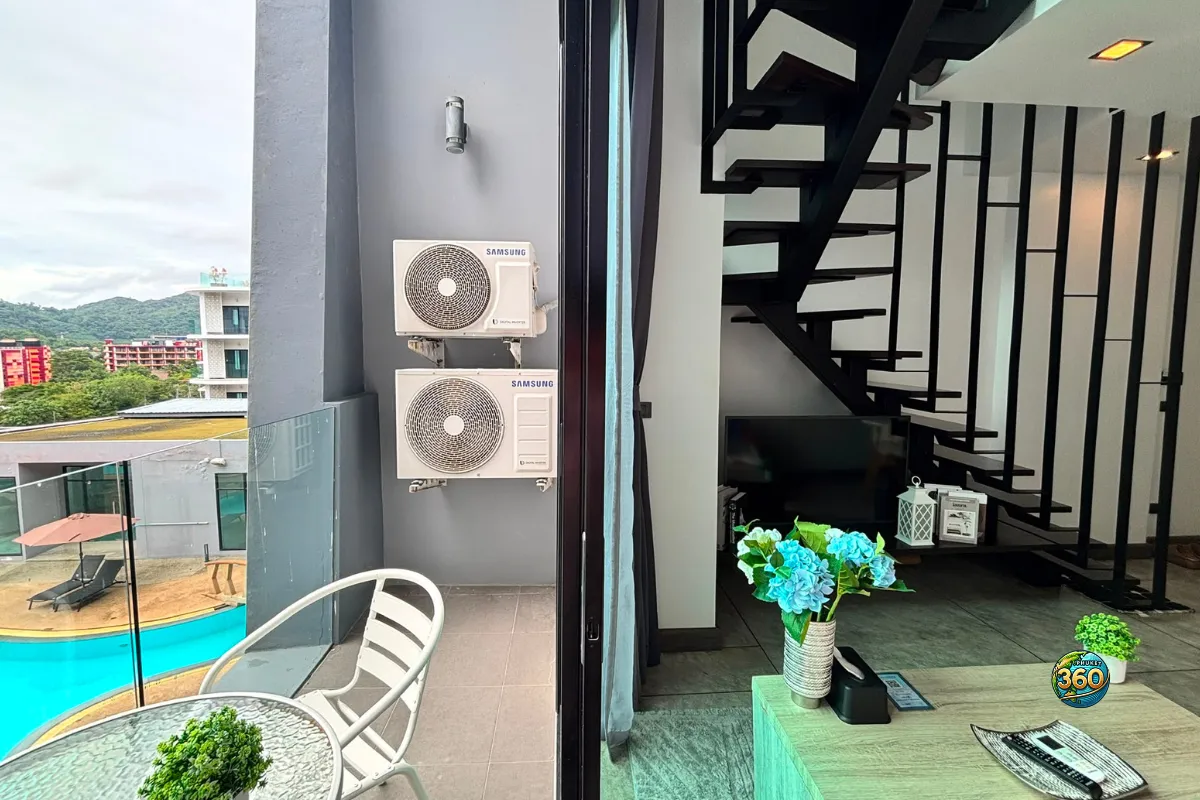 Vue depuis le balcon du duplex à Utopia Nai Harn, Phuket, avec table extérieure, salon intérieur et escalier noir