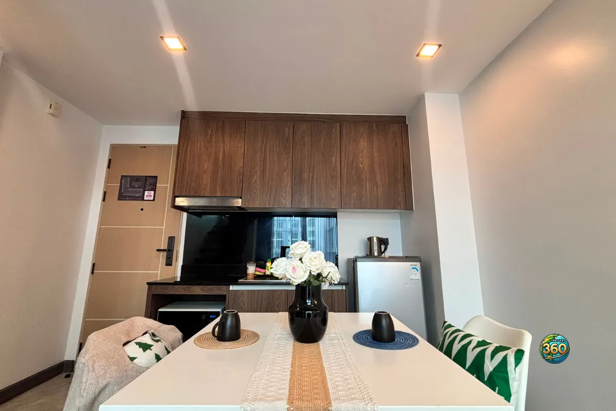 Coin repas du duplex à Utopia Nai Harn, Phuket, avec table blanche, chaises, cuisine équipée, réfrigérateur et rangements en bois