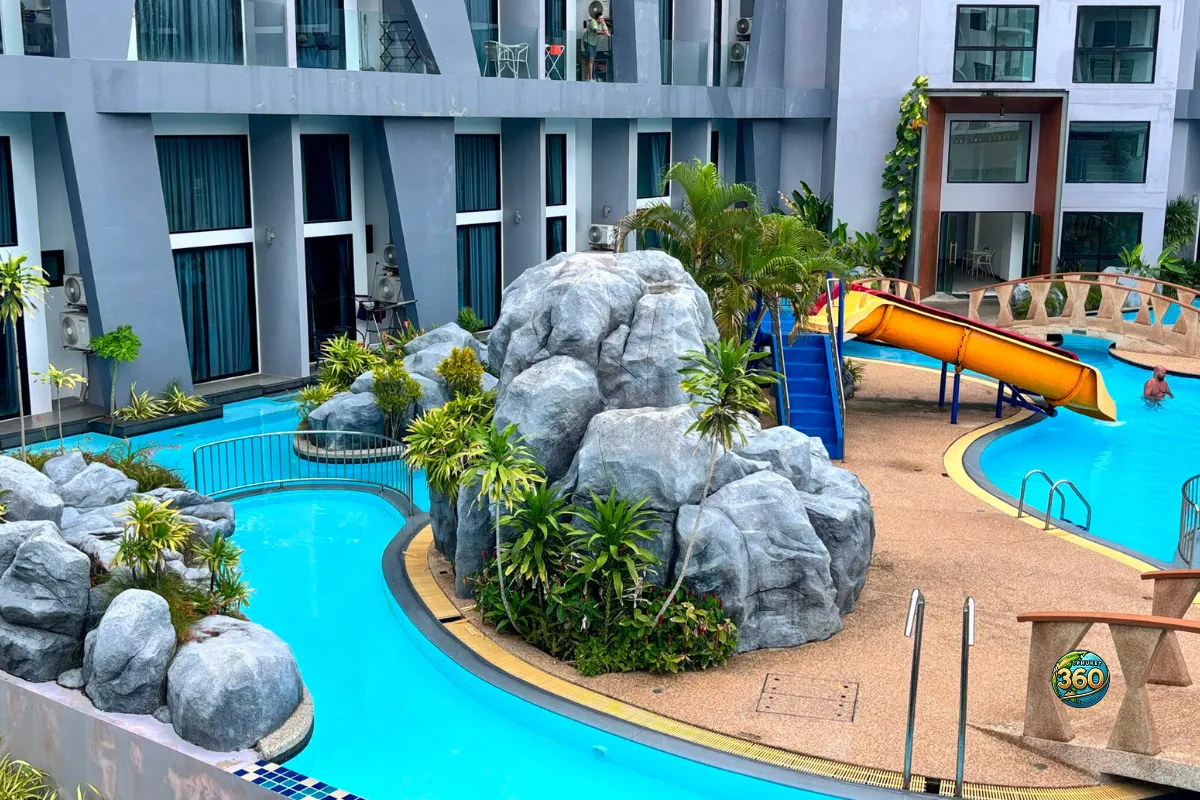 Piscine de la résidence Utopia Nai Harn à Phuket avec faux rochers, végétation, pont et toboggan orange