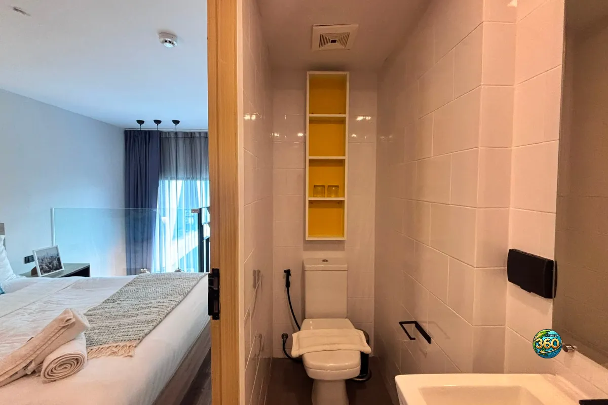 Salle de bain du duplex à Utopia Nai Harn, Phuket, avec toilettes, lavabo, carrelage blanc et étagère murale jaune