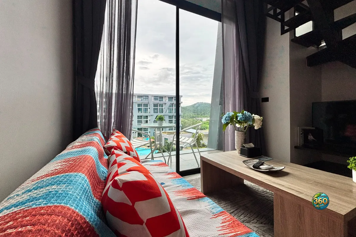 Salon lumineux du duplex à Utopia Nai Harn, Phuket, avec canapé coloré, table basse, grande baie vitrée et vue vers le balcon