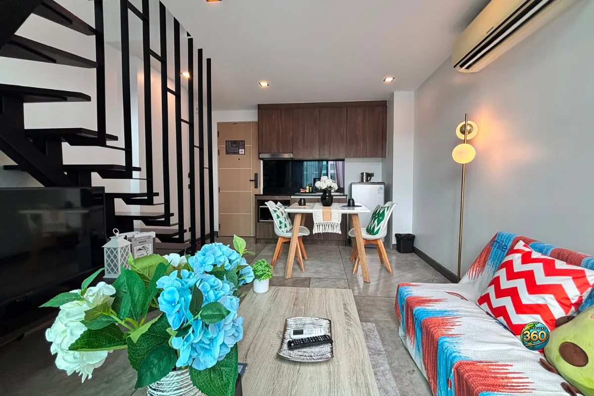 Salon du duplex moderne style loft à Utopia Nai Harn, Phuket, avec canapé coloré, escalier noir, coin repas et cuisine ouverte