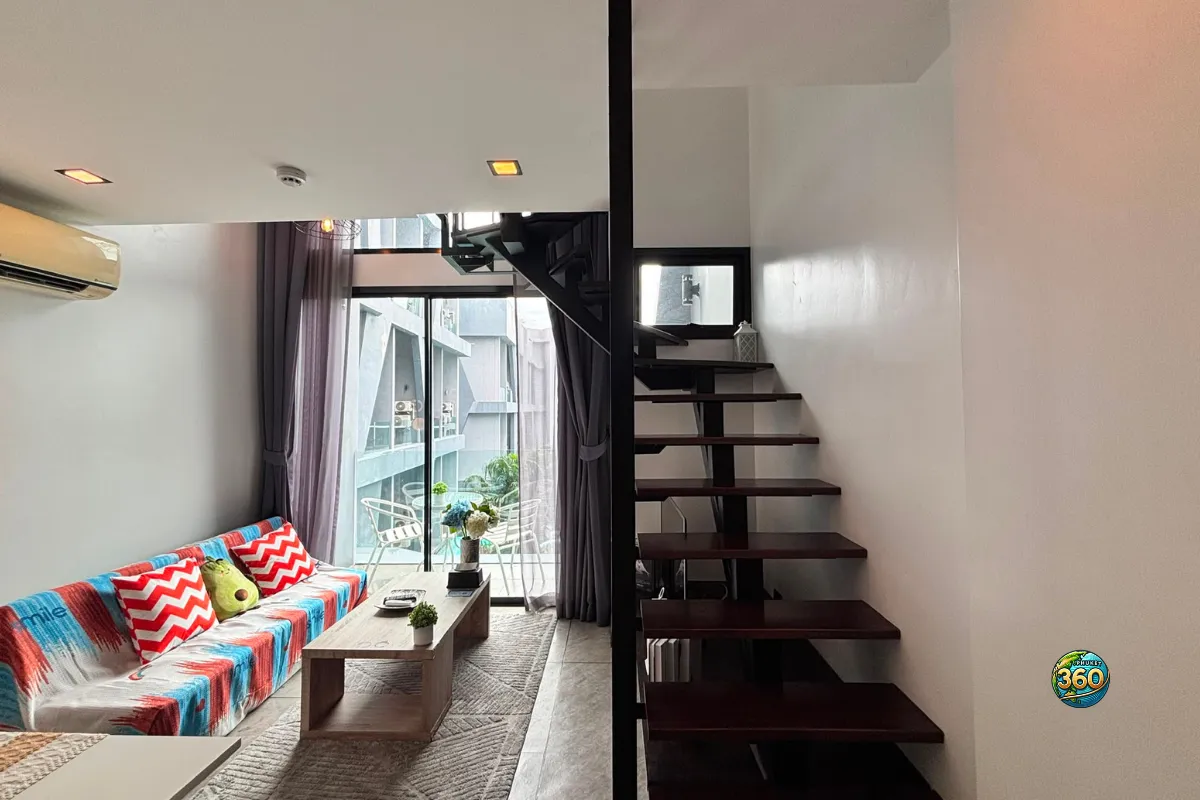 Salon du duplex moderne à Utopia Nai Harn, Phuket, avec canapé coloré, table basse, baie vitrée et escalier intérieur