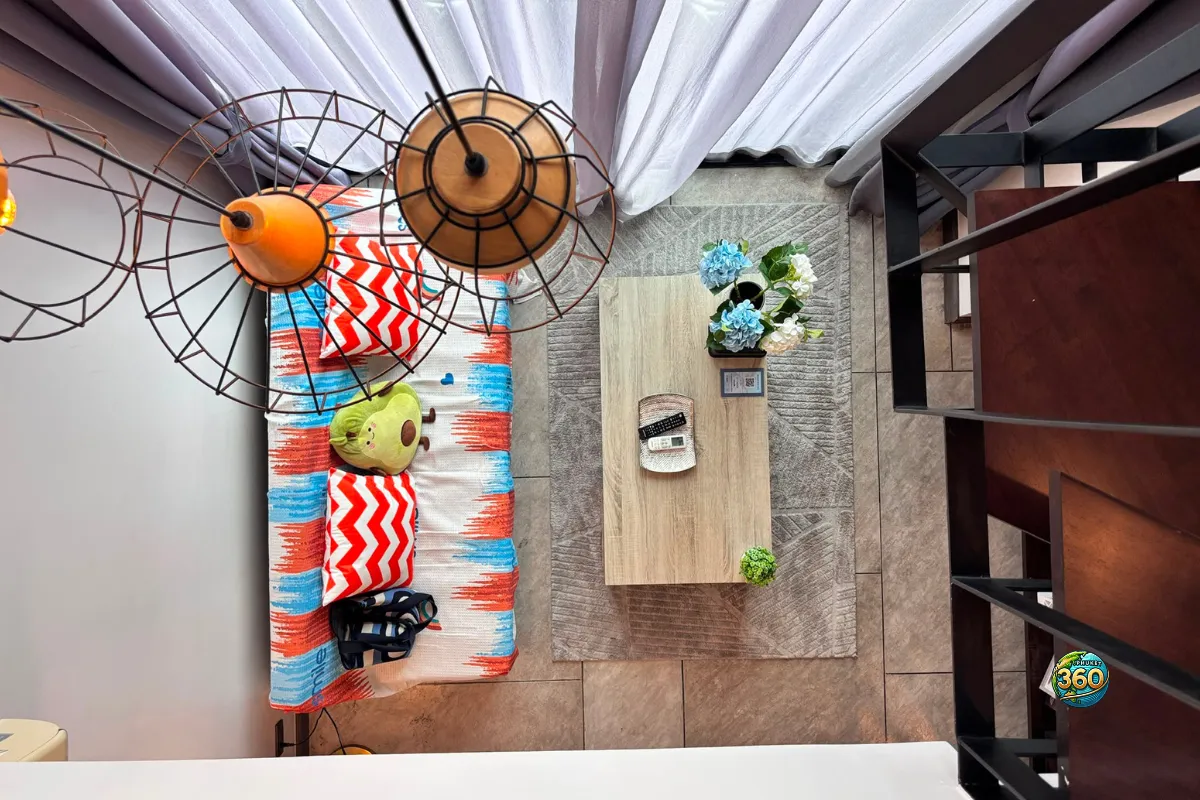 Vue en plongée sur le salon du duplex à Utopia Nai Harn, Phuket, avec canapé coloré, table basse, tapis et escalier