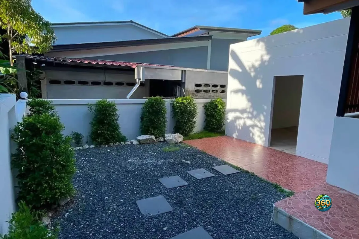 Cour extérieure de la maison 3 chambres à louer à Bang Tao, Phuket, avec sol en gravier, plantes, terrasse carrelée et mur de clôture
