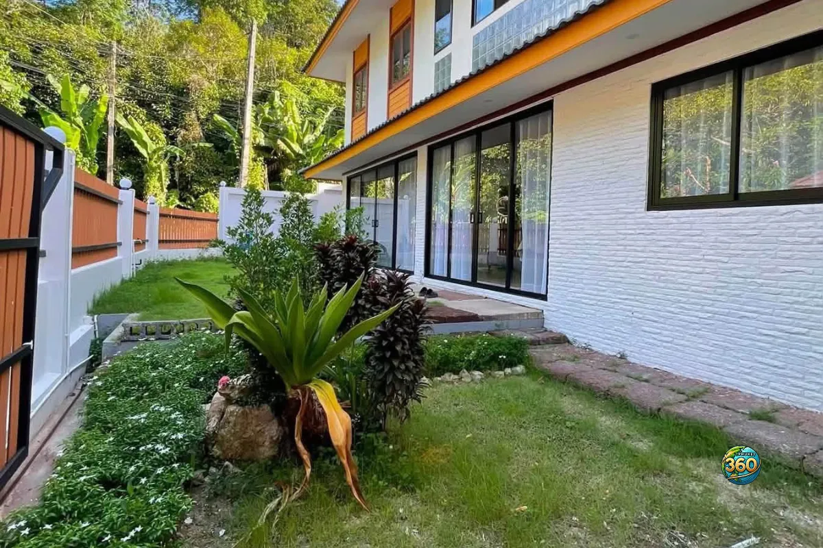 Jardin latéral de la maison 3 chambres à louer à Bang Tao, Phuket, avec façade vitrée, plantes, pelouse et clôture