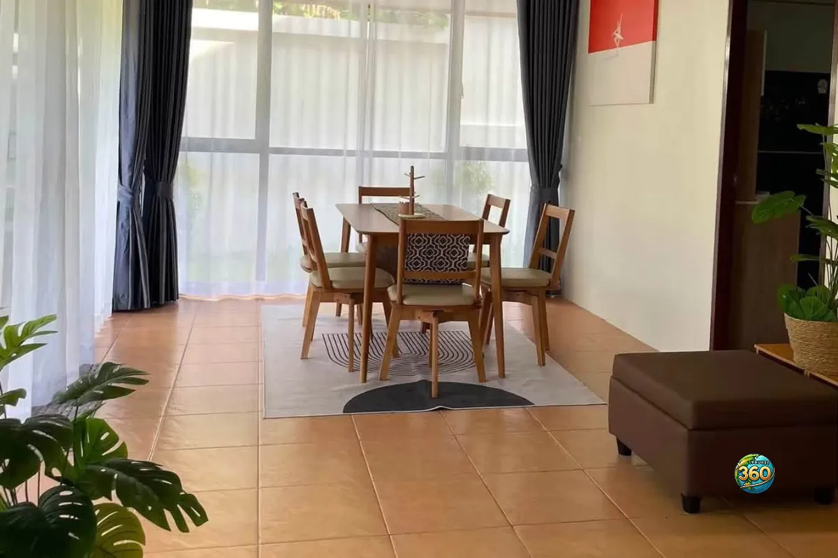 Salle à manger de la maison 3 chambres à louer à Bang Tao, Phuket, avec table en bois, chaises, grandes baies vitrées et vue sur le jardin