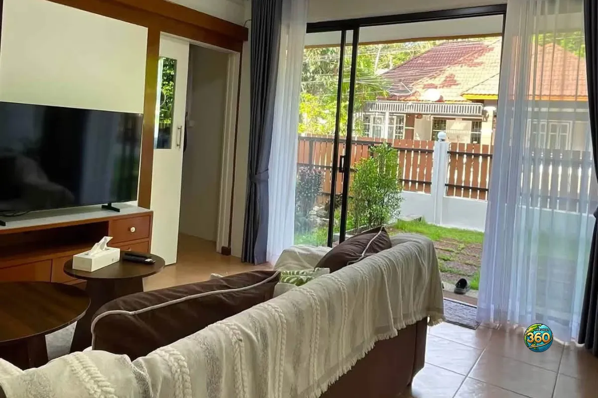 Salon de la maison 3 chambres à louer à Bang Tao, Phuket, avec canapé, télévision, baie vitrée et vue directe sur le jardin