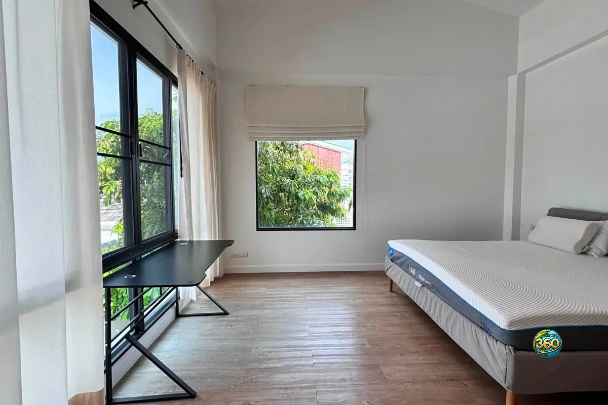 Chambre lumineuse de la maison Mono Plus Palai à Phuket avec lit, bureau près des fenêtres, rideaux et sol imitation bois