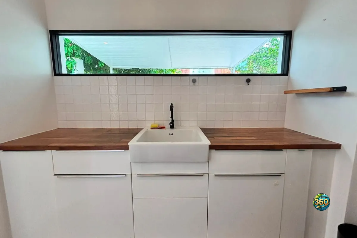 Cuisine de la maison Mono Plus Palai à Phuket avec évier blanc, robinet noir, plan de travail en bois et fenêtre horizontale