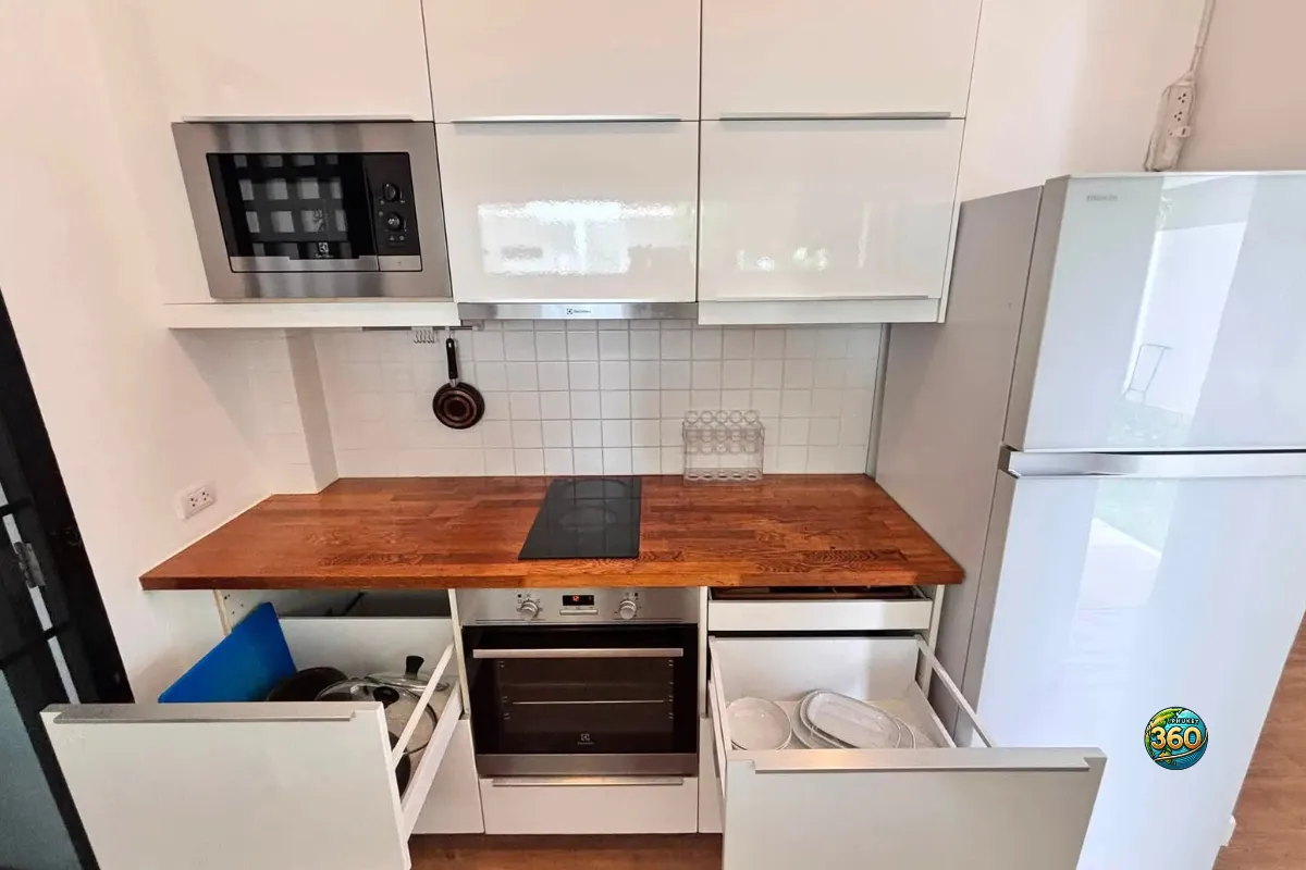 Cuisine équipée de la maison Mono Plus Palai à Phuket avec micro-ondes, four, plaque de cuisson, réfrigérateur, rangements ouverts et vaisselle