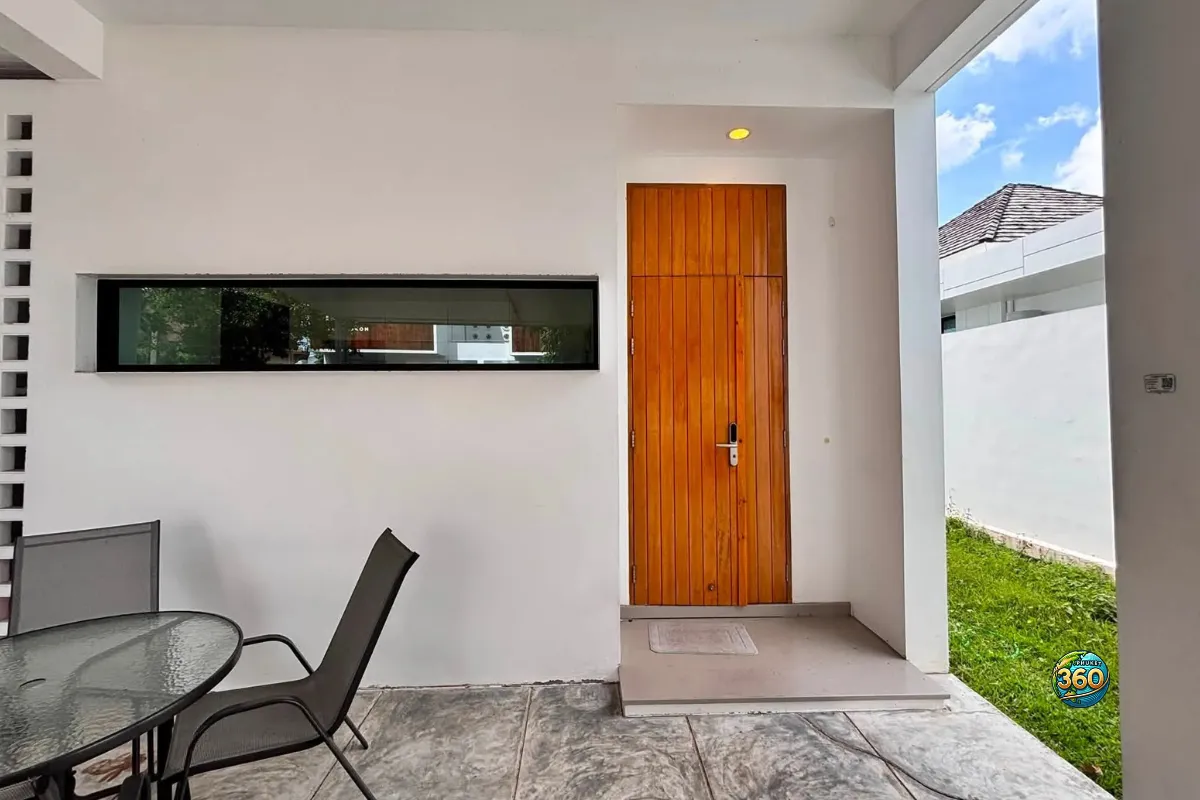 Entrée de la maison Mono Plus Palai à Phuket avec porte en bois, terrasse couverte, table extérieure et petit jardin latéral
