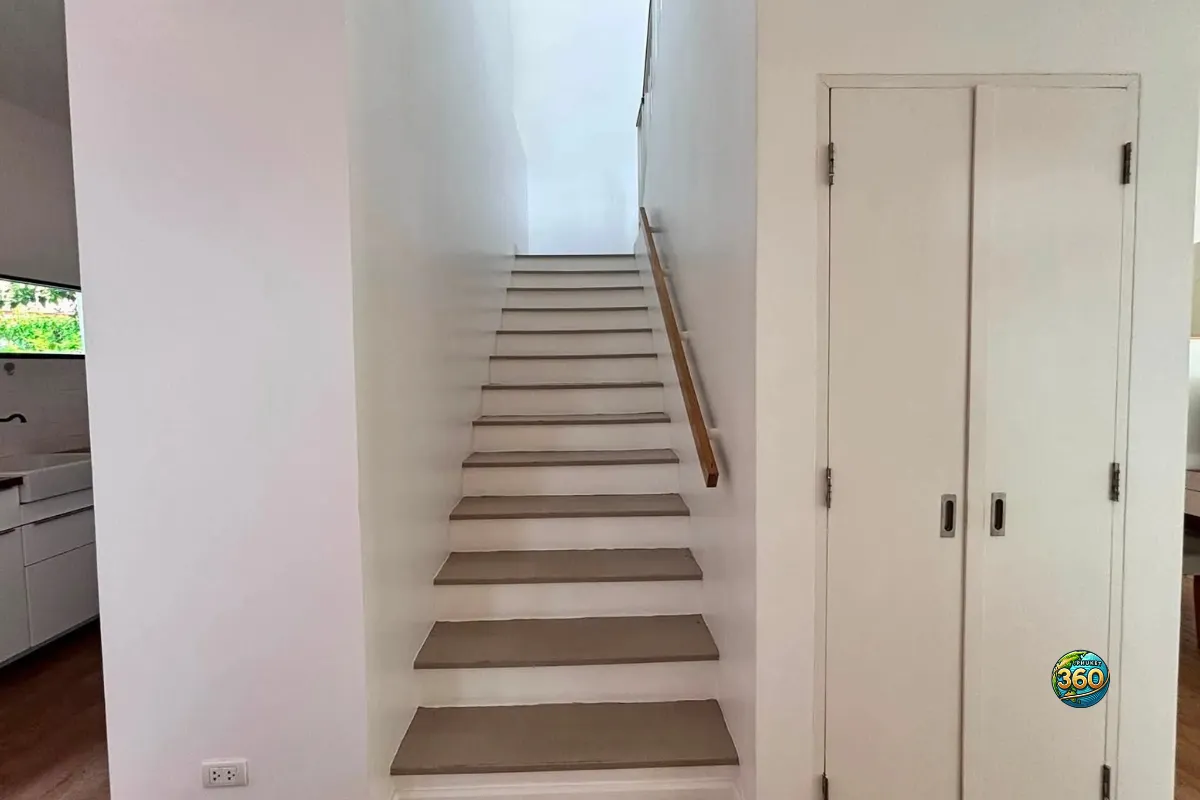 Escalier intérieur de la maison Mono Plus Palai à Phuket avec rampe en bois, mur blanc et placard intégré
