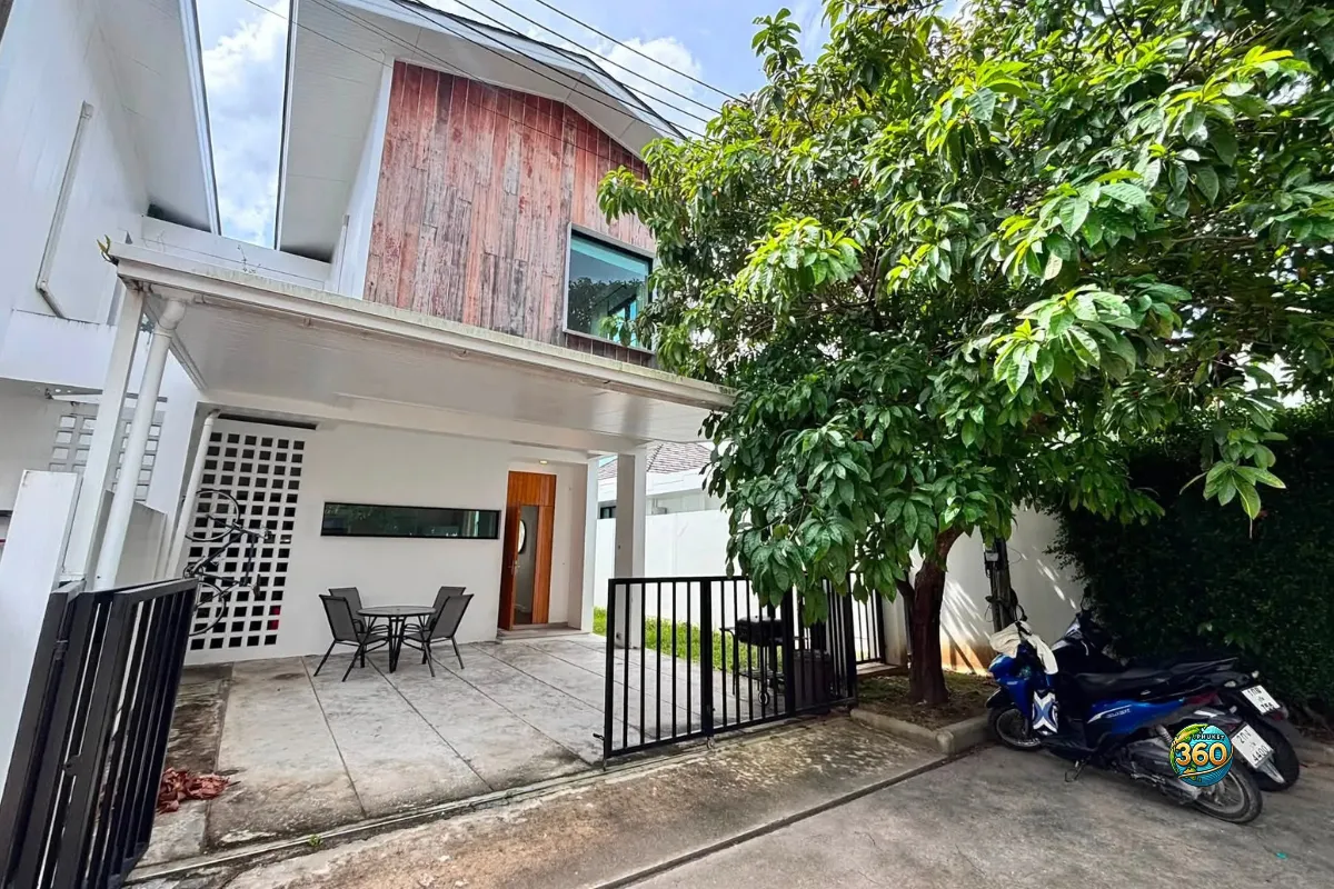 Façade extérieure de la maison Mono Plus Palai à Phuket avec terrasse couverte, portail, arbre dans la cour et scooters devant l’entrée