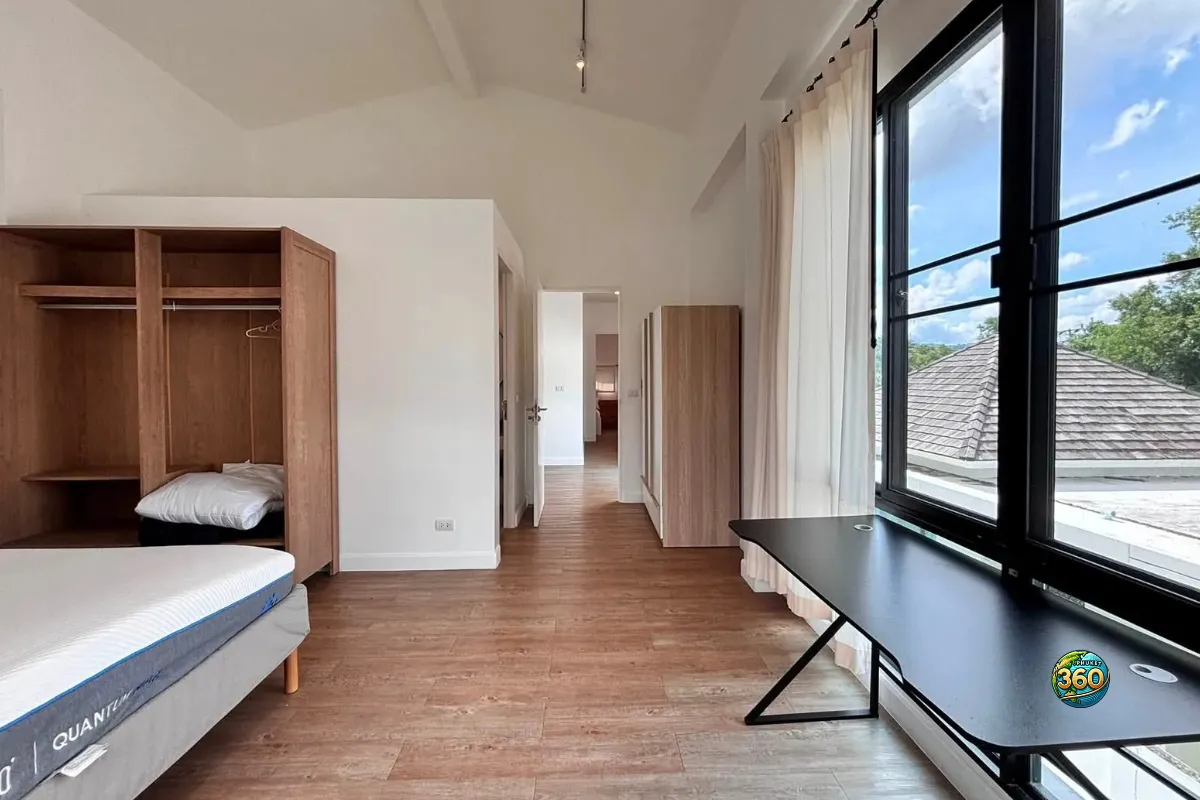 Grande chambre de la maison Mono Plus Palai à Phuket avec lit, armoire ouverte, bureau près de la fenêtre, rideaux et sol imitation bois