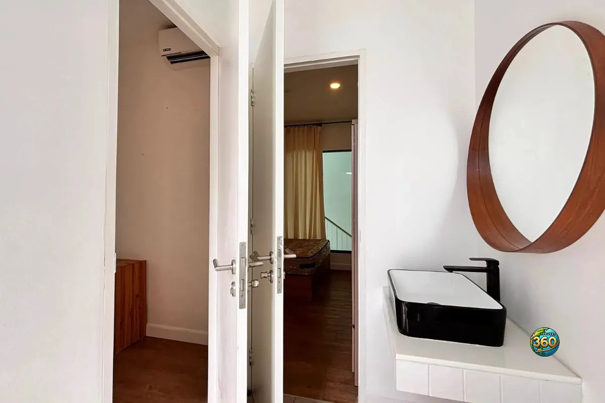 Vue depuis la salle de bain à l’étage de la maison Mono Plus Palai à Phuket, avec lavabo moderne, miroir rond et accès aux chambres