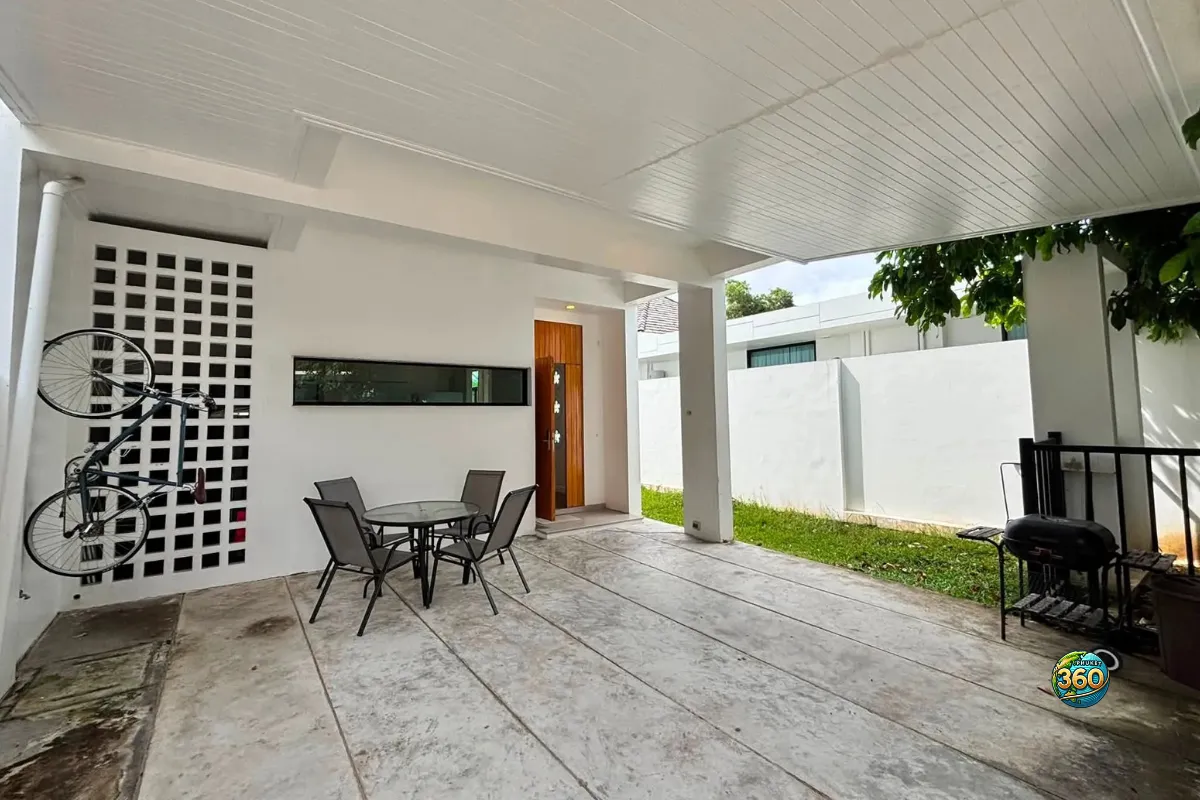 Terrasse couverte de la maison Mono Plus Palai à Phuket avec table extérieure, vélo mural, barbecue et petit jardin latéral