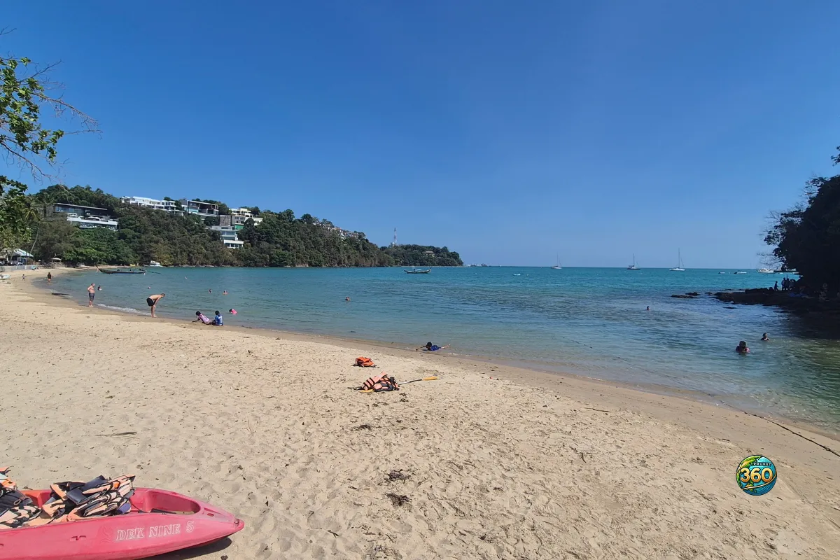 Plage de sable à Ao Yon Beach à Phuket, avec une mer turquoise, des baigneurs et des bateaux au large