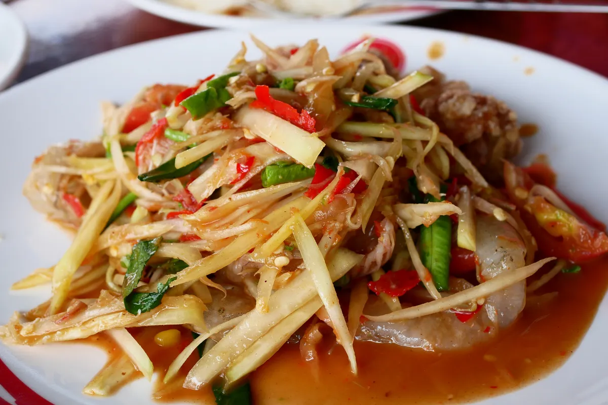 Assiette de som tam thaï avec papaye verte râpée, crevettes, piments rouges, haricots longs, tomate et sauce épicée