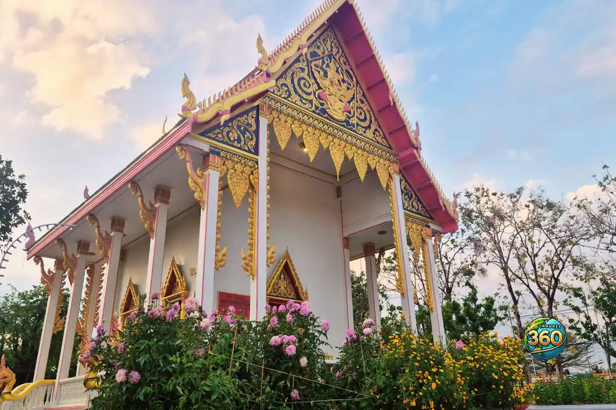 Pavillon blanc et doré entouré de fleurs colorées dans l’enceinte du Wat Chalong à Phuket